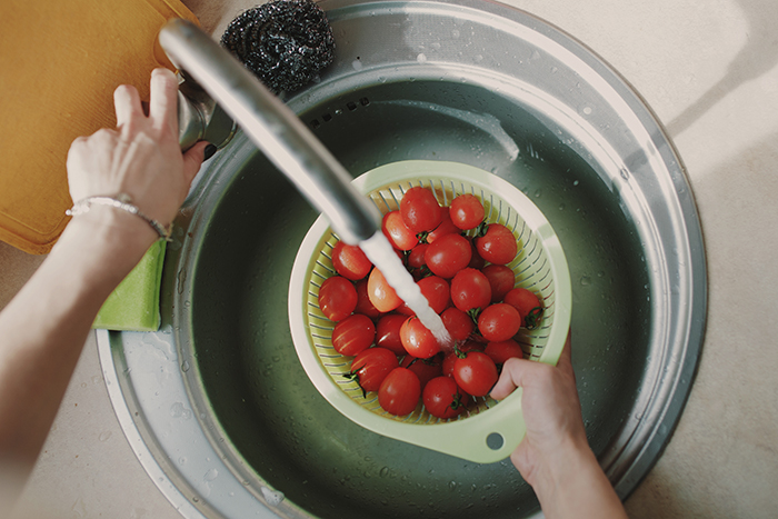 Torneira ligada lavando tomates cereja em uma pia de cozinha 