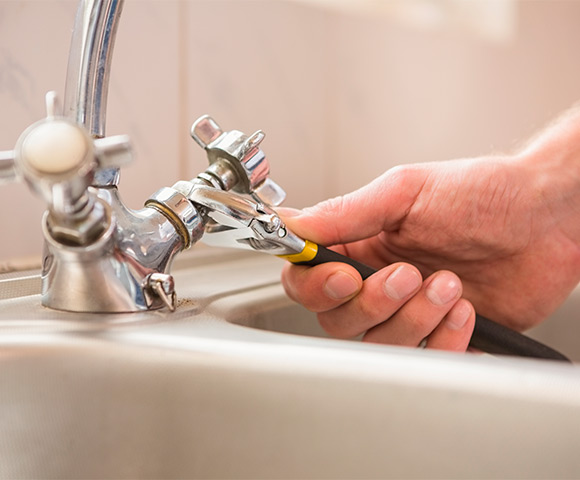 Mão masculina consertando uma torneira vazando